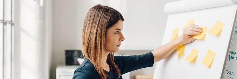 Young woman sticking yellow sticky notes to flip chart at office